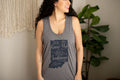 A woman wearing a heather gray racerback tank top with a navy blue graphic of the state of Indiana and the text 'She Grew Up in an Indiana Town'.